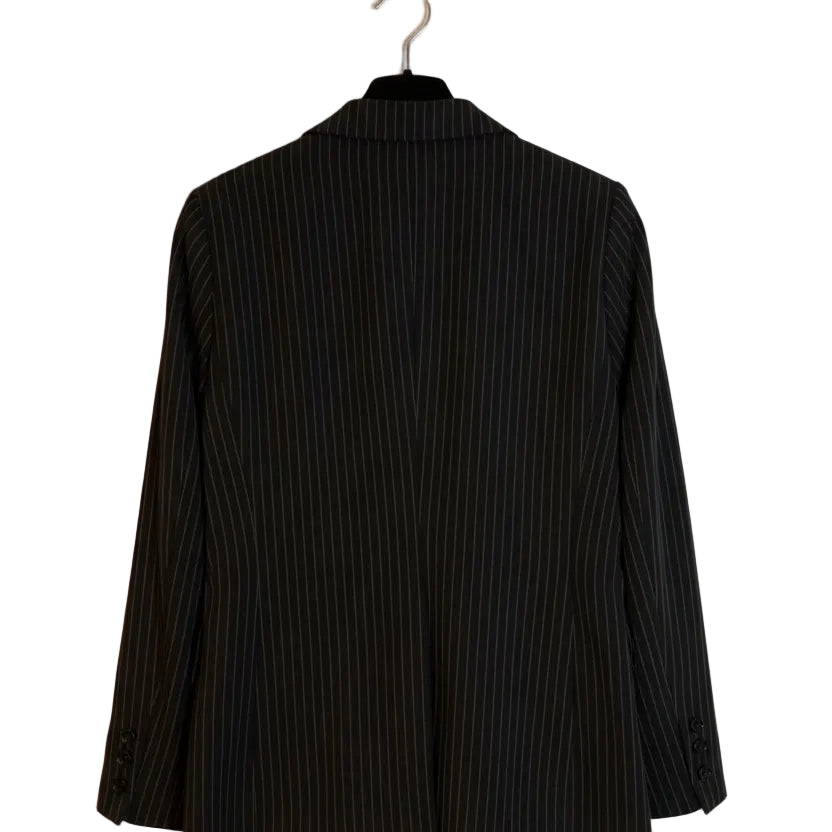 A black pinstripe blazer jacket hanging on a black hanger against a plain off-white wall.
