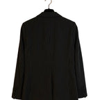A black pinstripe blazer jacket hanging on a black hanger against a plain off-white wall.