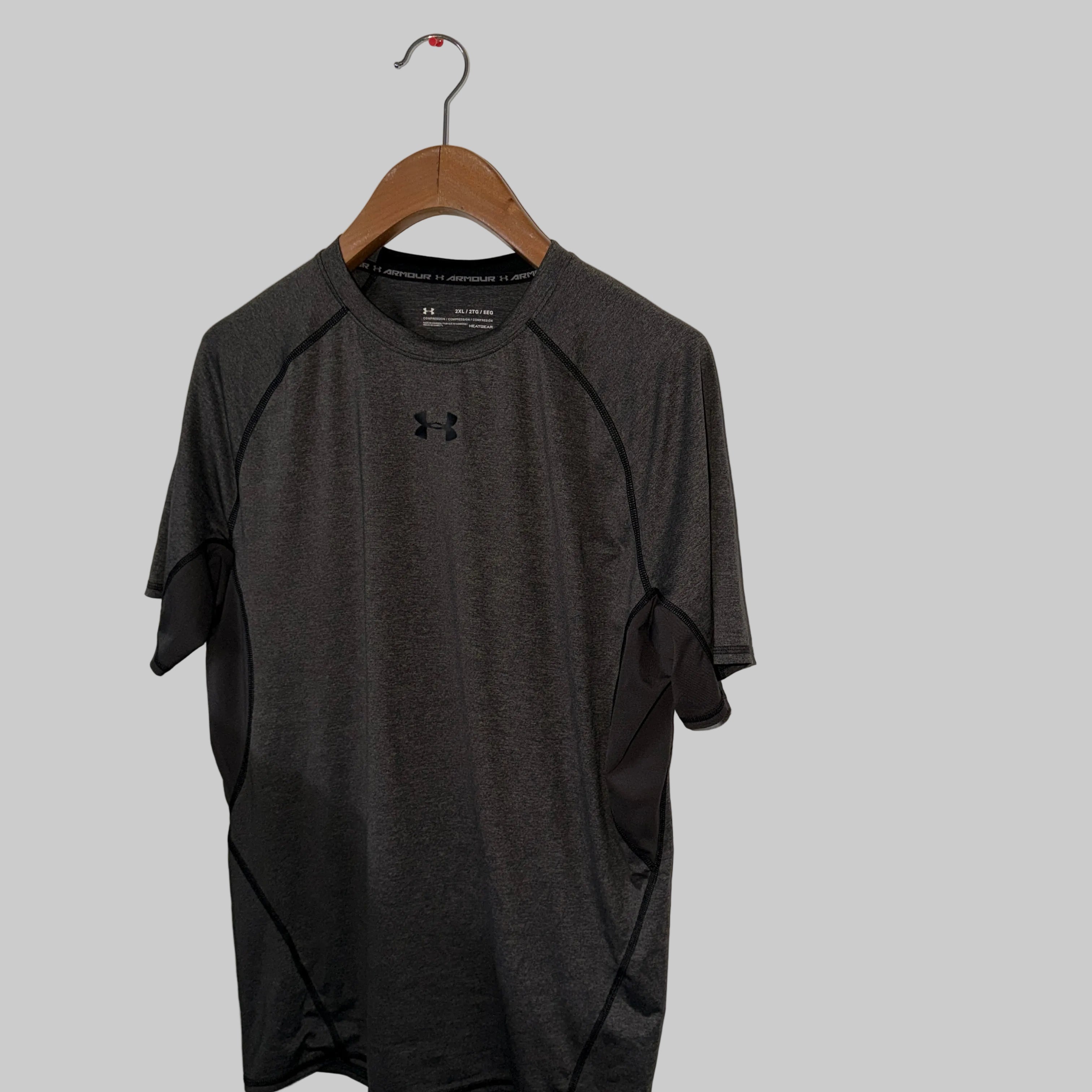 Gray t-shirt with Under Armour logo on a wooden hanger against a white wall.