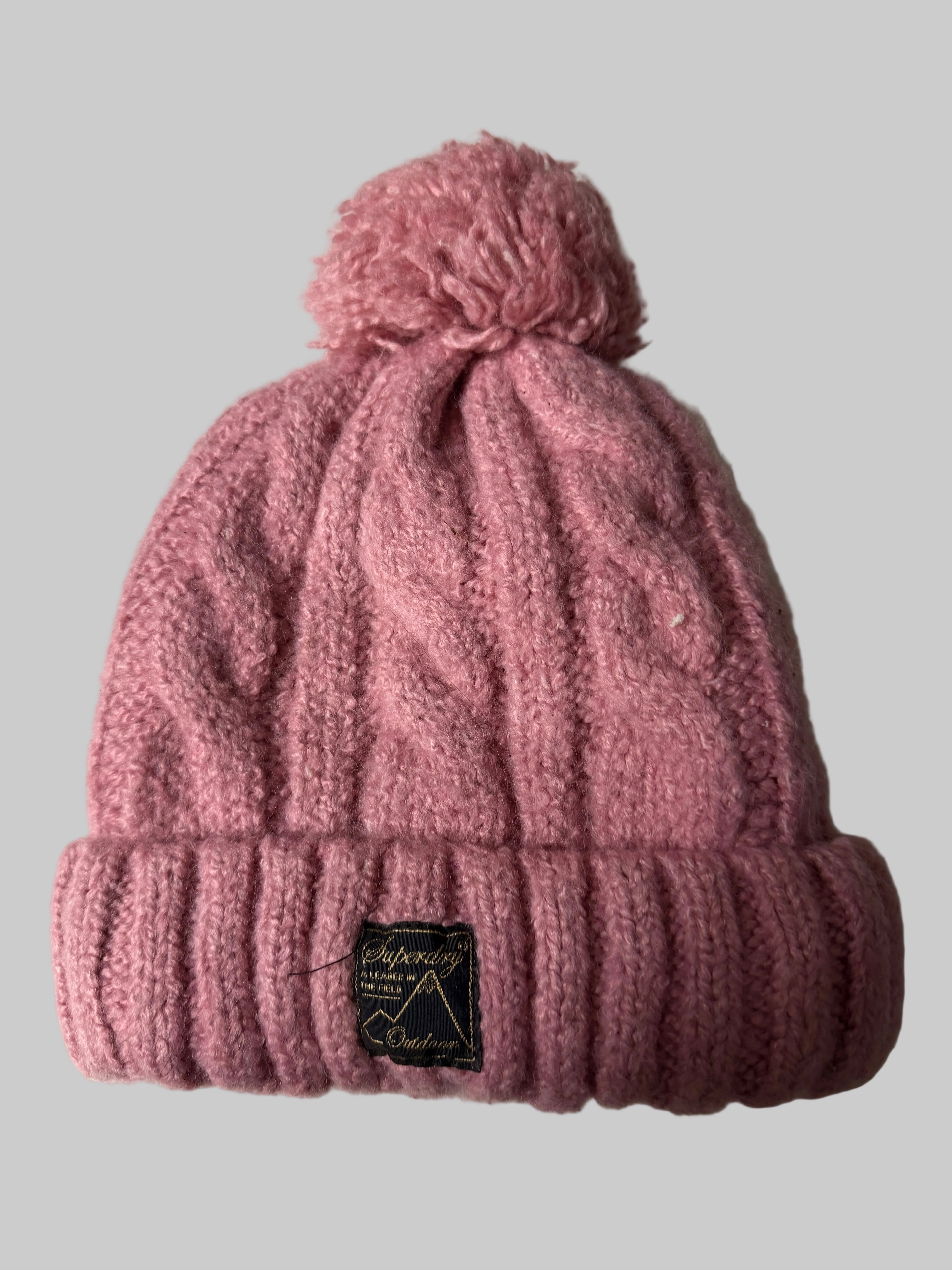 Pink knitted beanie with a brand label on a white surface