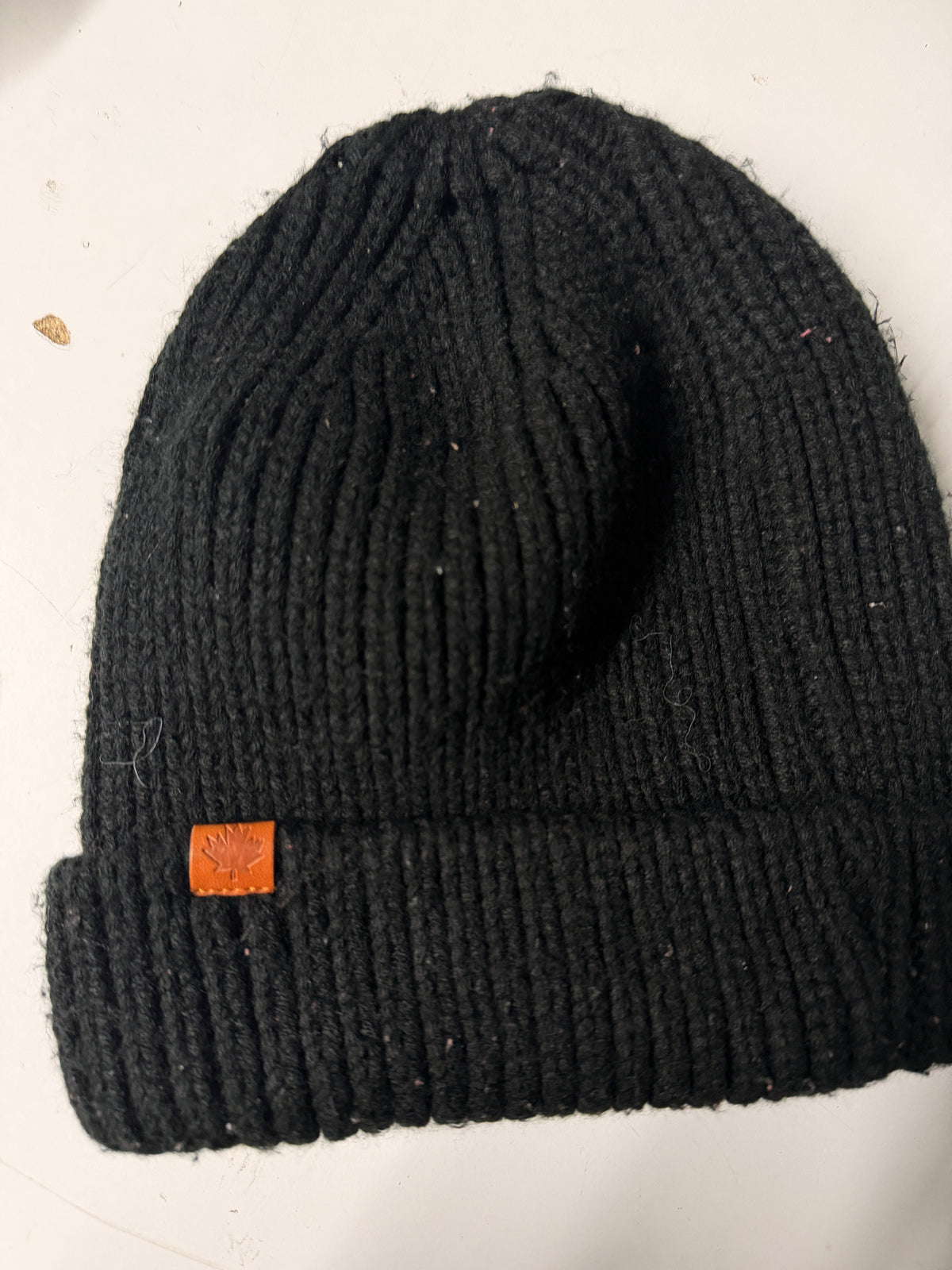 Black knit beanie with a brown logo tag on a white surface KU 7307
