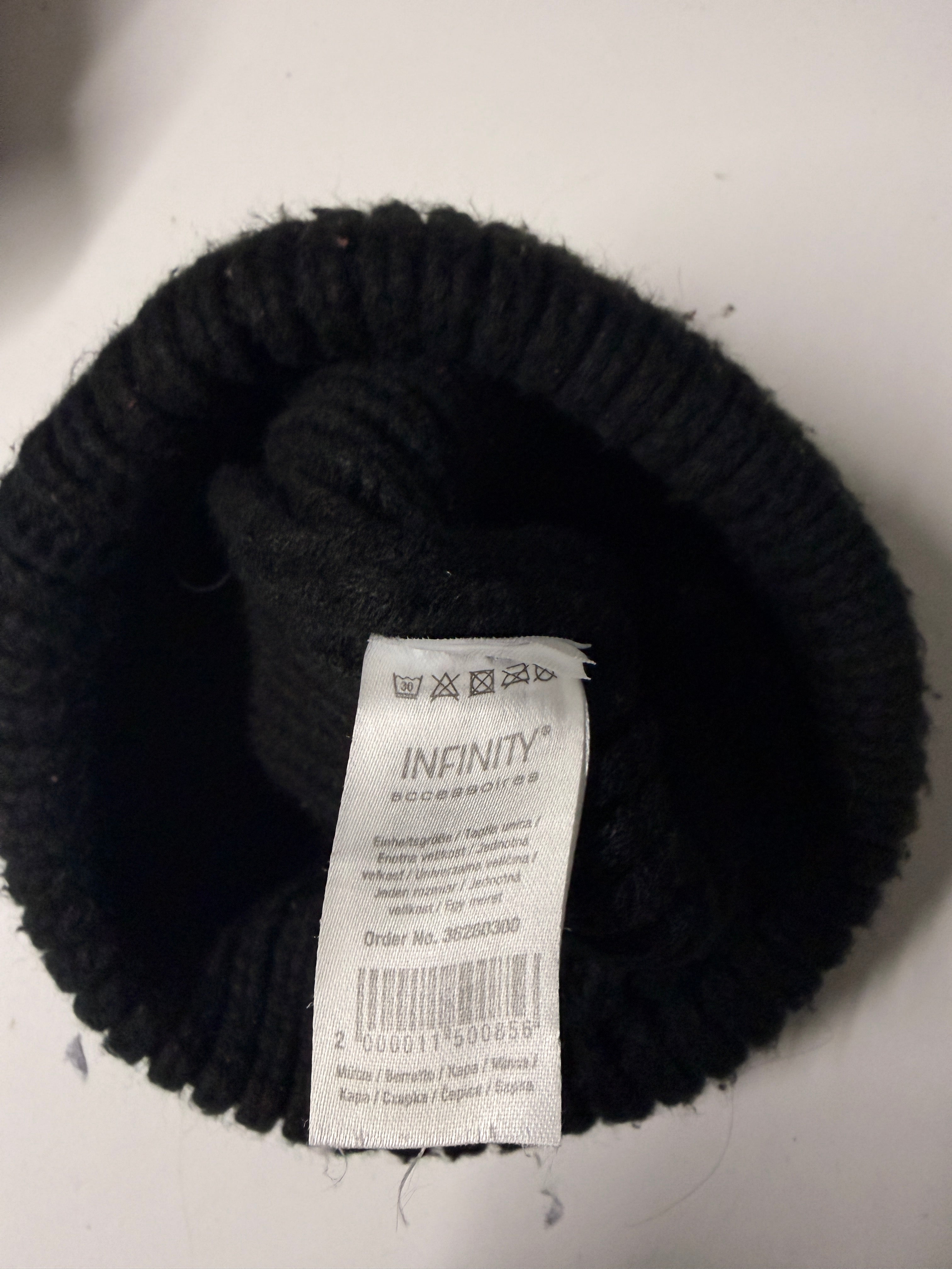 Black knit beanie with a brown logo tag on a white surface KU 7307