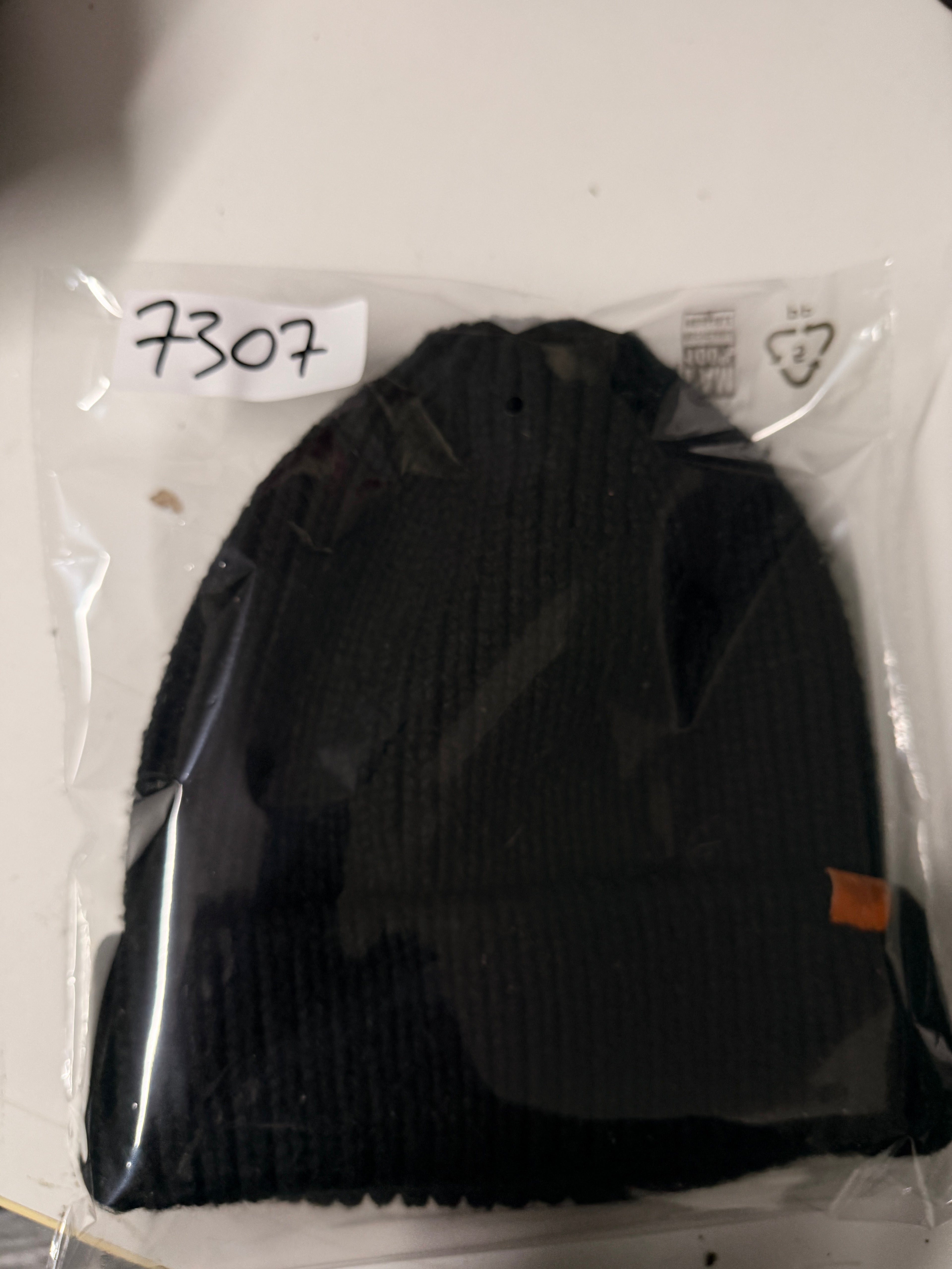 Black knit beanie with a brown logo tag on a white surface KU 7307