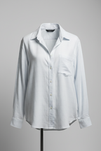 A white oversized long sleeve men's shirt hanging on a hanger against an orange background.
