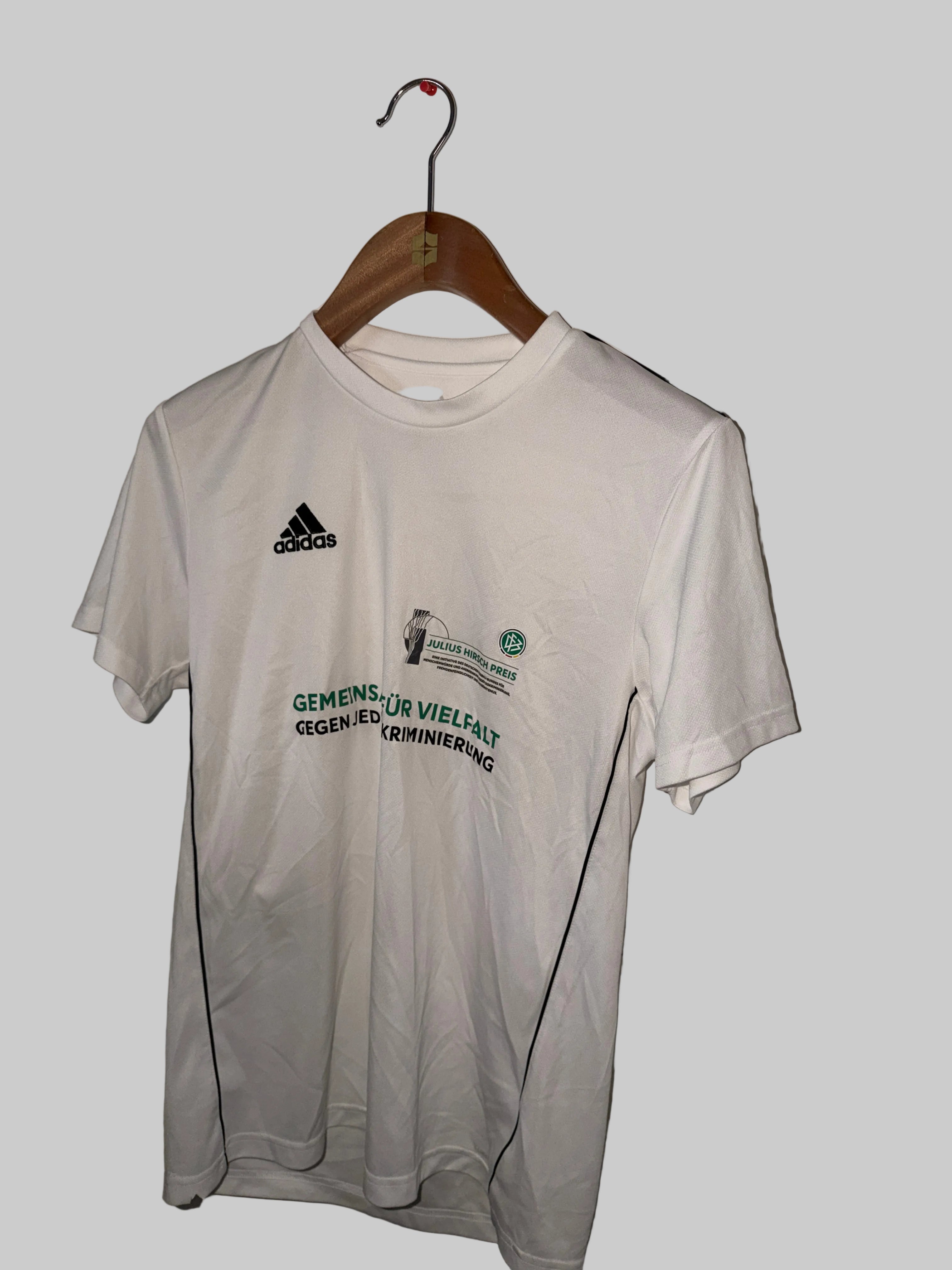 White t-shirt with green text and Adidas logo on a hanger against a white background
