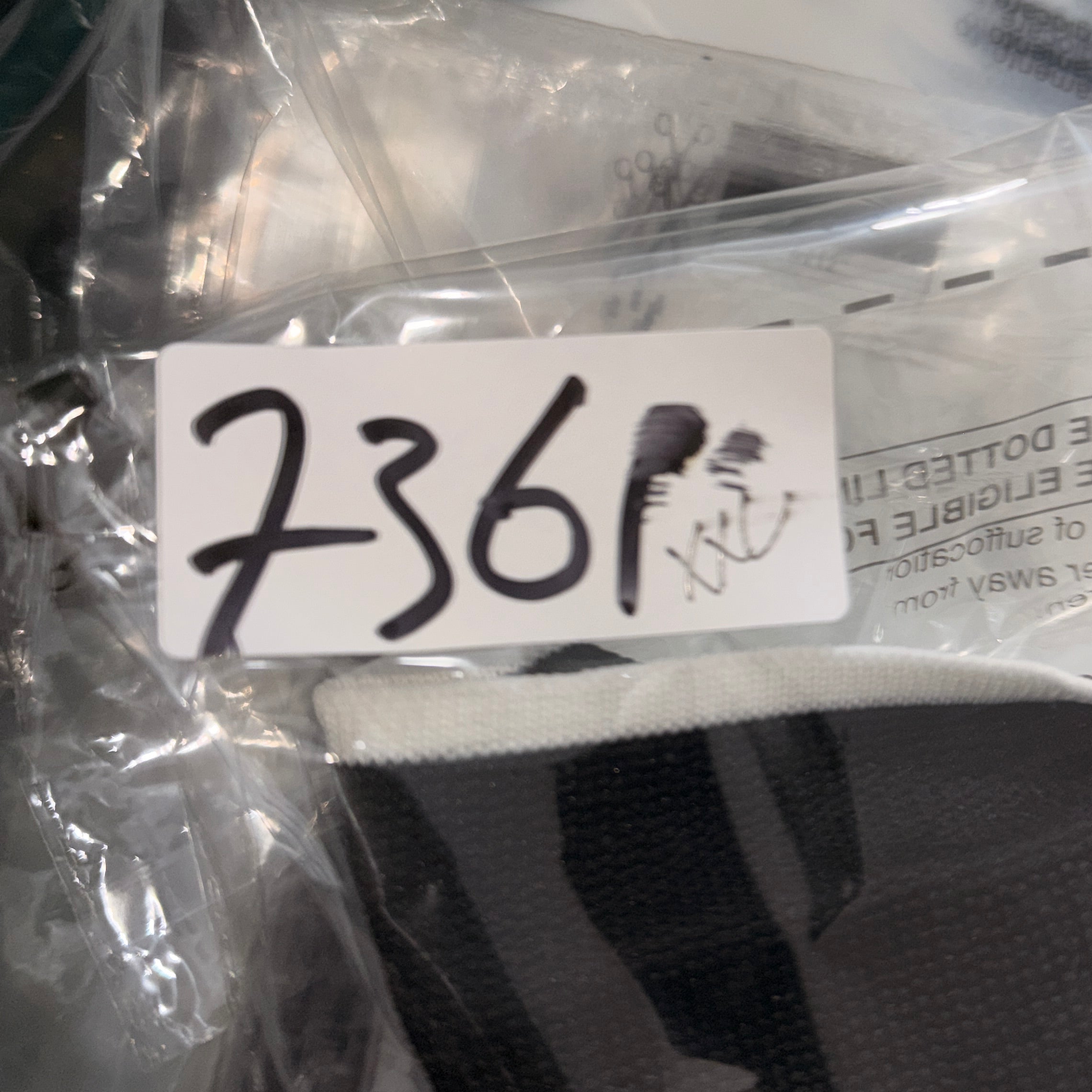 Black cap with a white tag displaying numbers, partially wrapped in clear plastic.