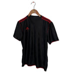 Black Adidas shirt with red accents on a hanger against a white wall.