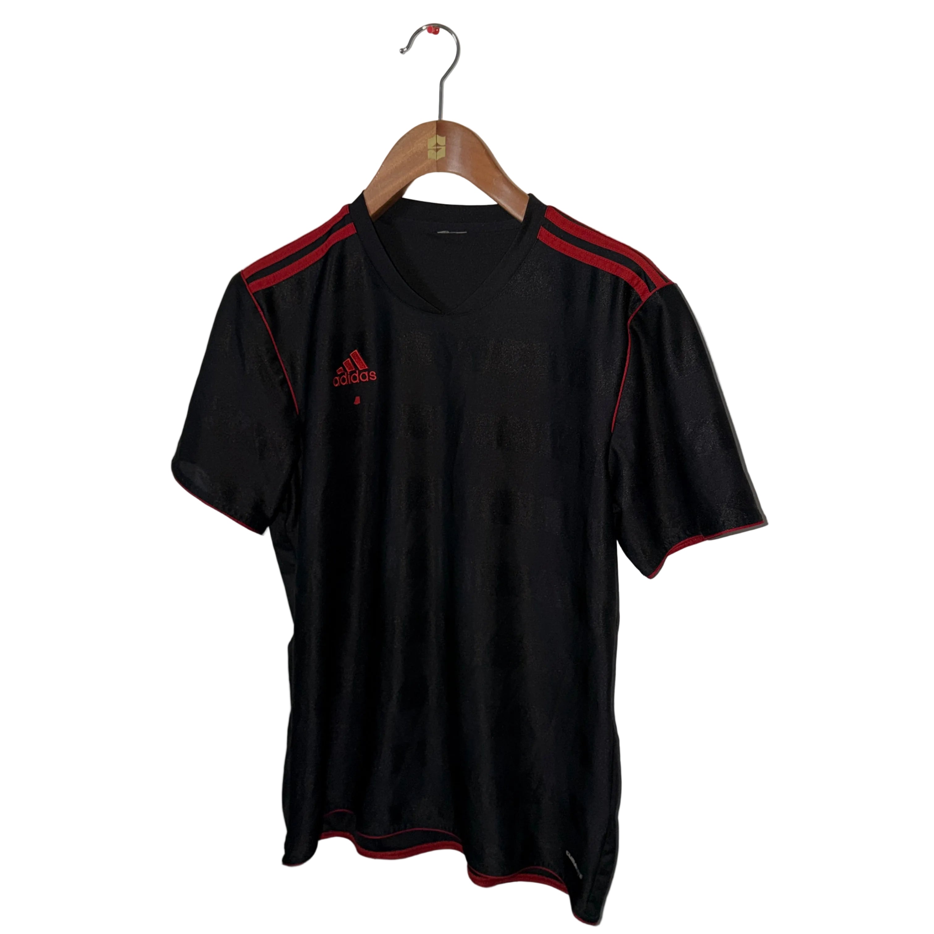 Black Adidas shirt with red accents on a hanger against a white wall.