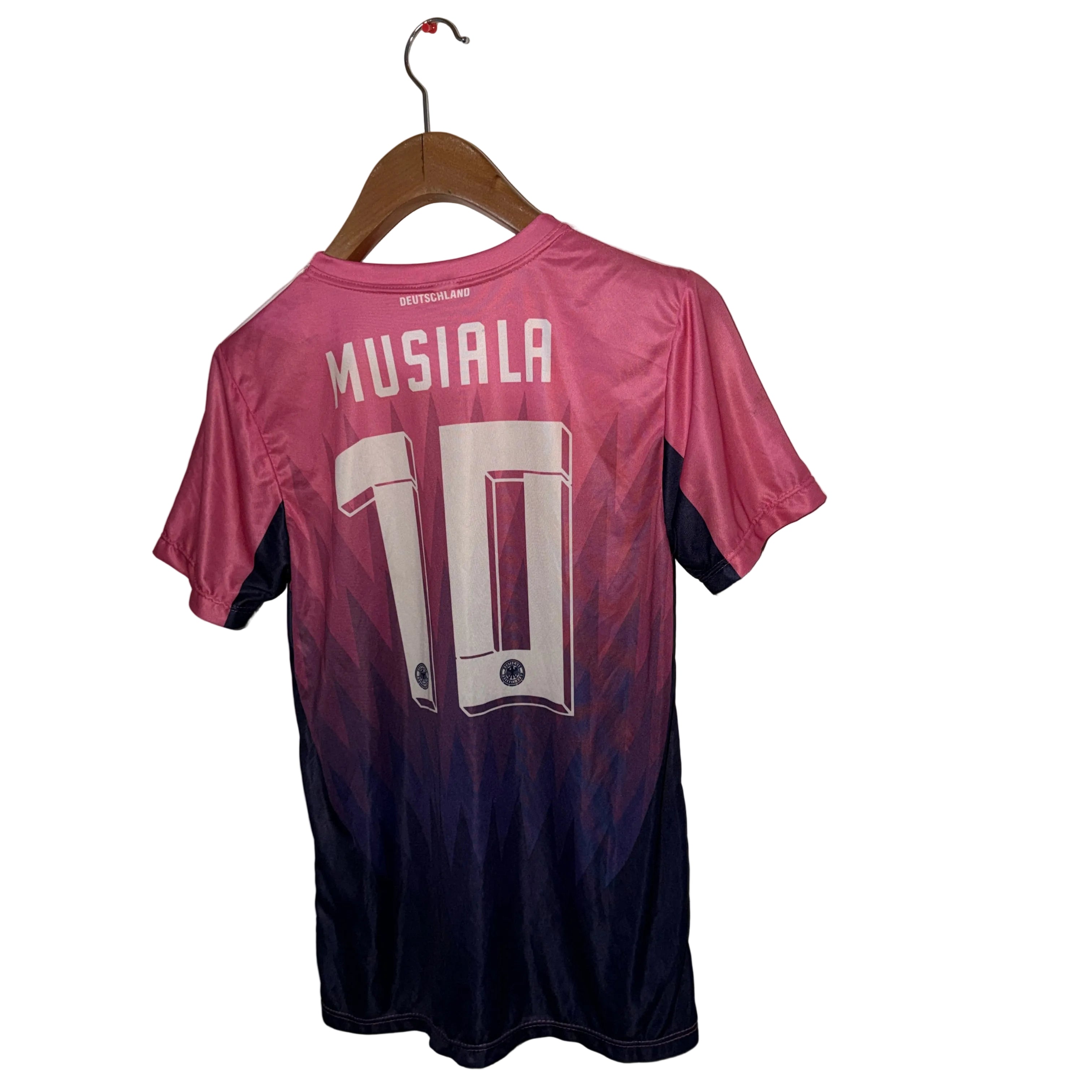 Pink and black sports jersey with 'Musiala' and number '10' on a hanger against a white wall.