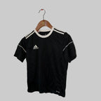 Black Adidas t-shirt on a hanger against a white wall.