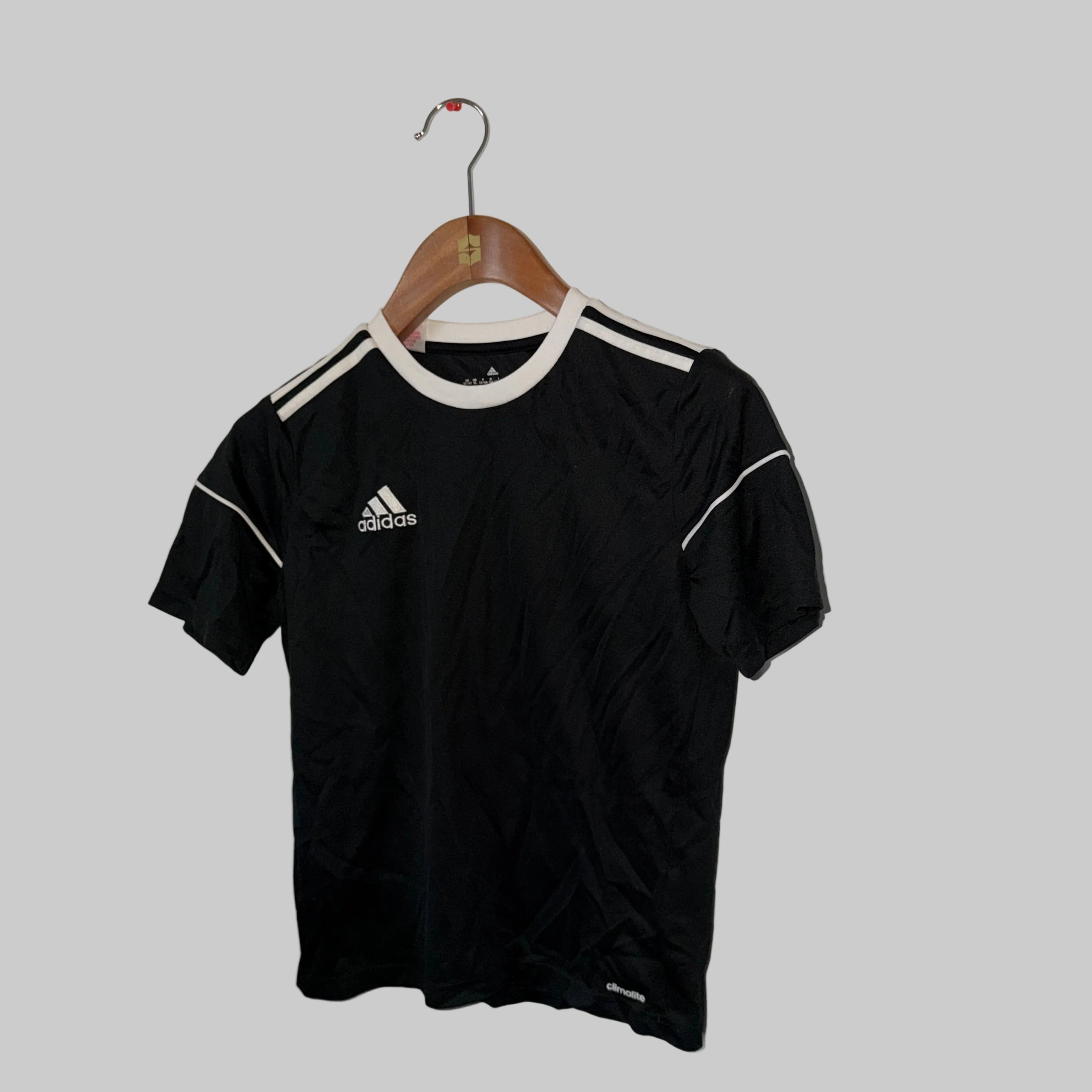 Black Adidas t-shirt on a hanger against a white wall.