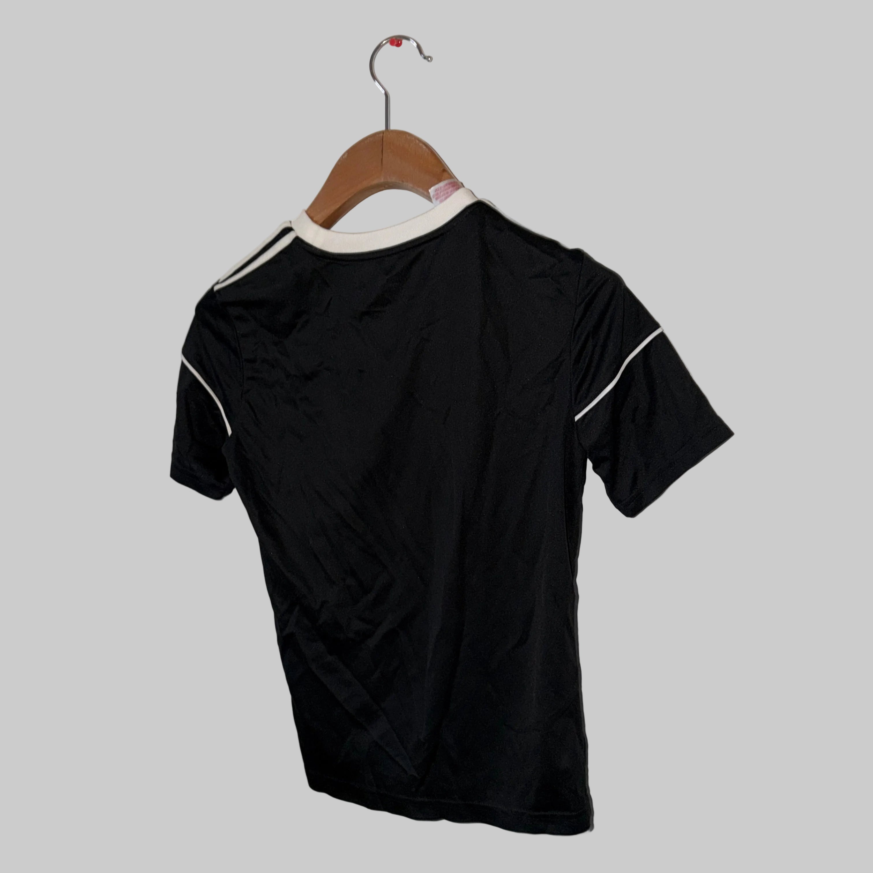 Black t-shirt with white accents on a hanger against a white wall.