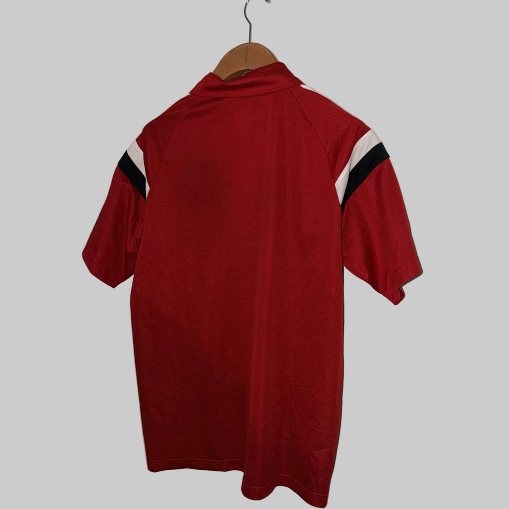 Red polo shirt with white and black stripes on a hanger against a white wall.