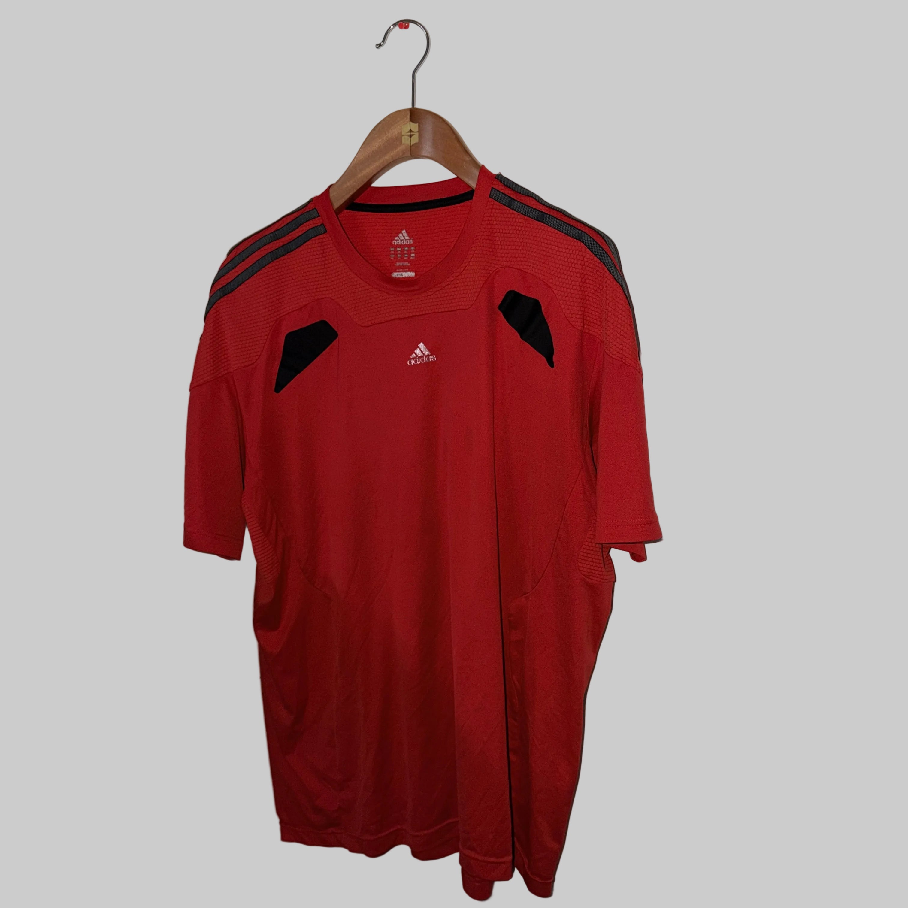 Red Adidas sports shirt on a hanger against a white wall.