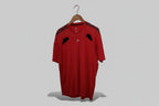 Red Adidas sports shirt on a hanger against a white wall.