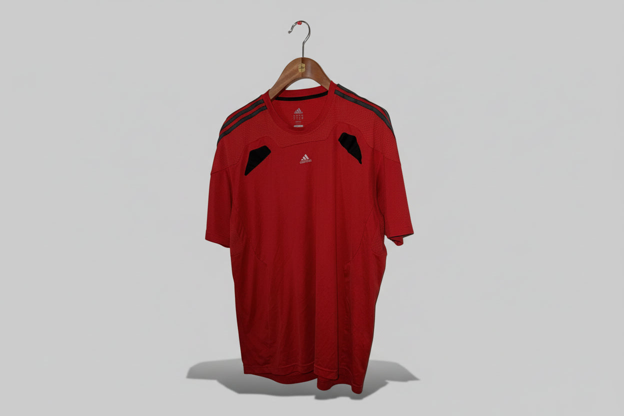 Red Adidas sports shirt on a hanger against a white wall.