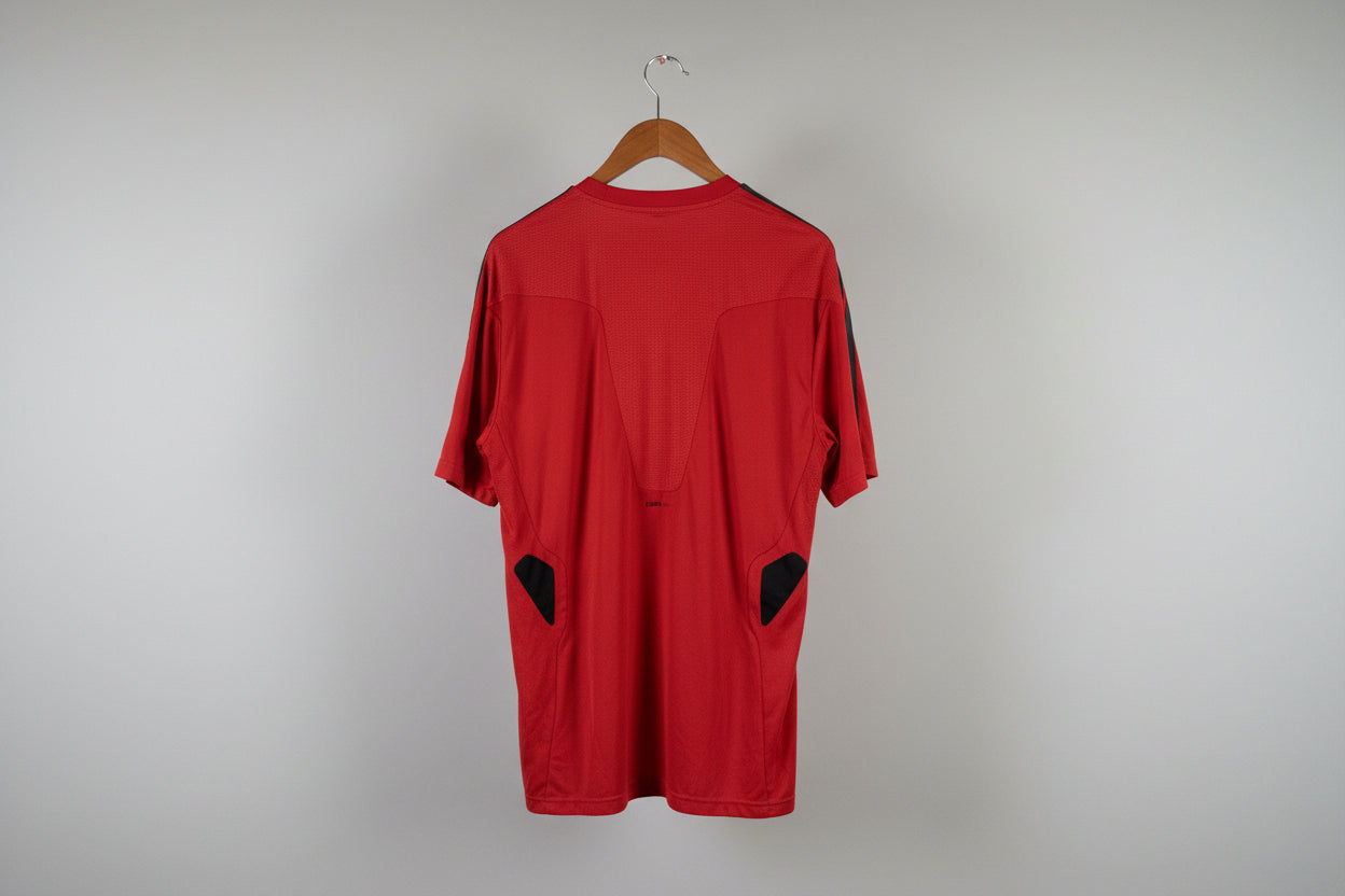 Red shirt with black accents on a hanger against a white wall.