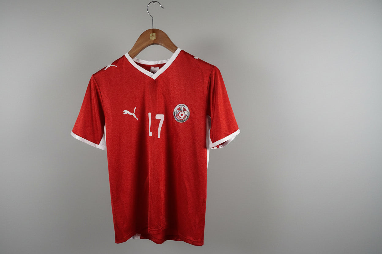 Red sports jersey with number 17 and logo on a hanger against a white wall.
