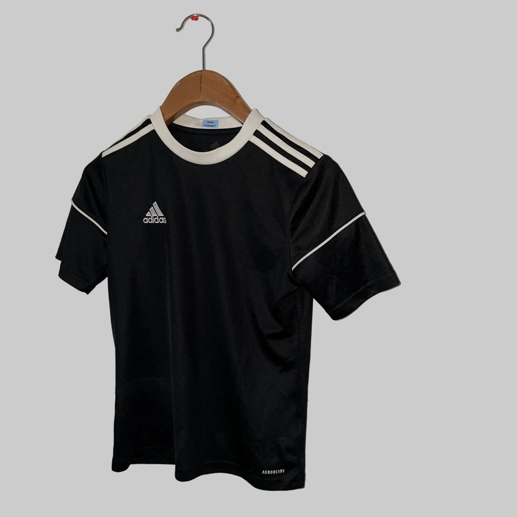 Black Adidas sports jersey with white accents on a wooden hanger against a white wall.