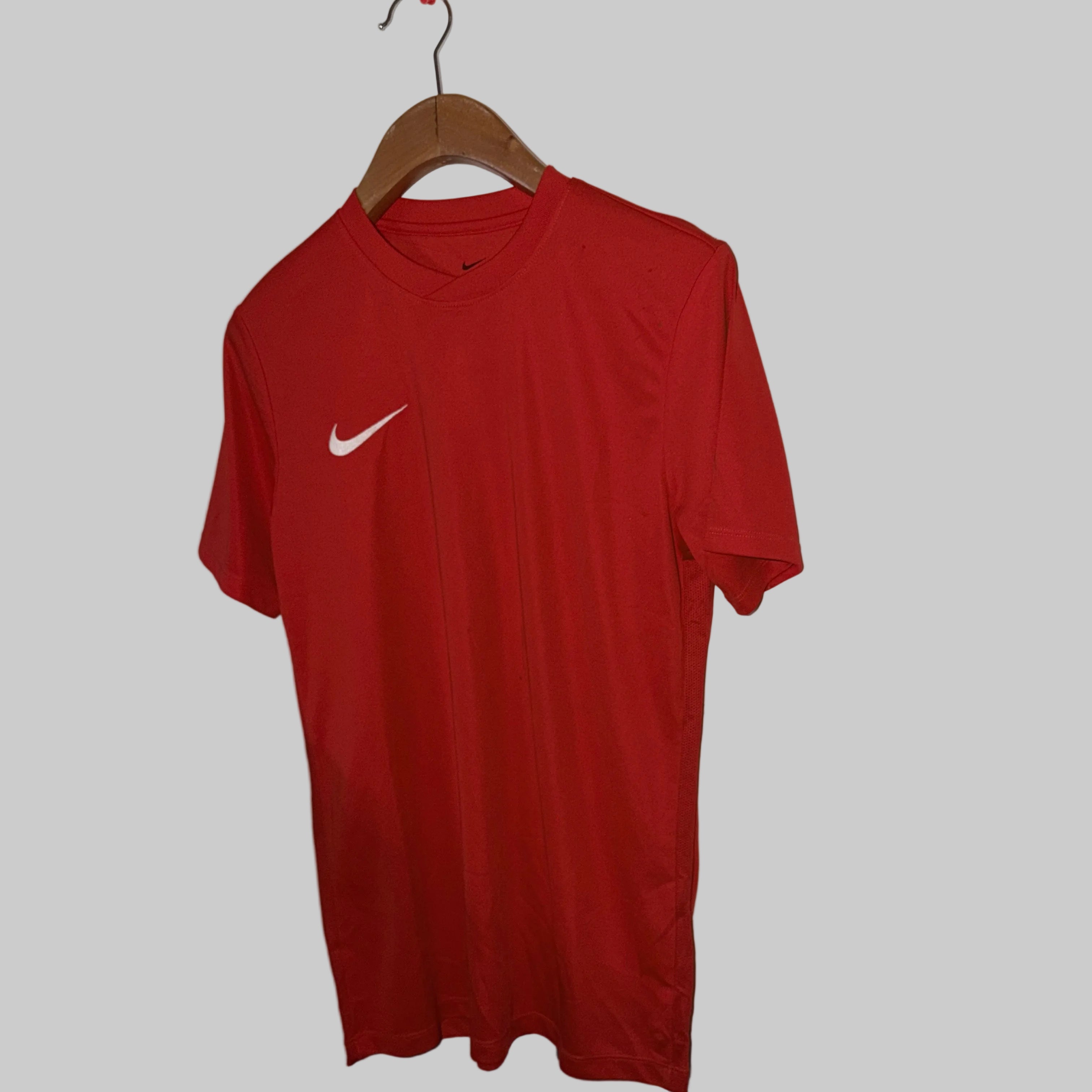 Red Nike t-shirt on a hanger against a white wall.