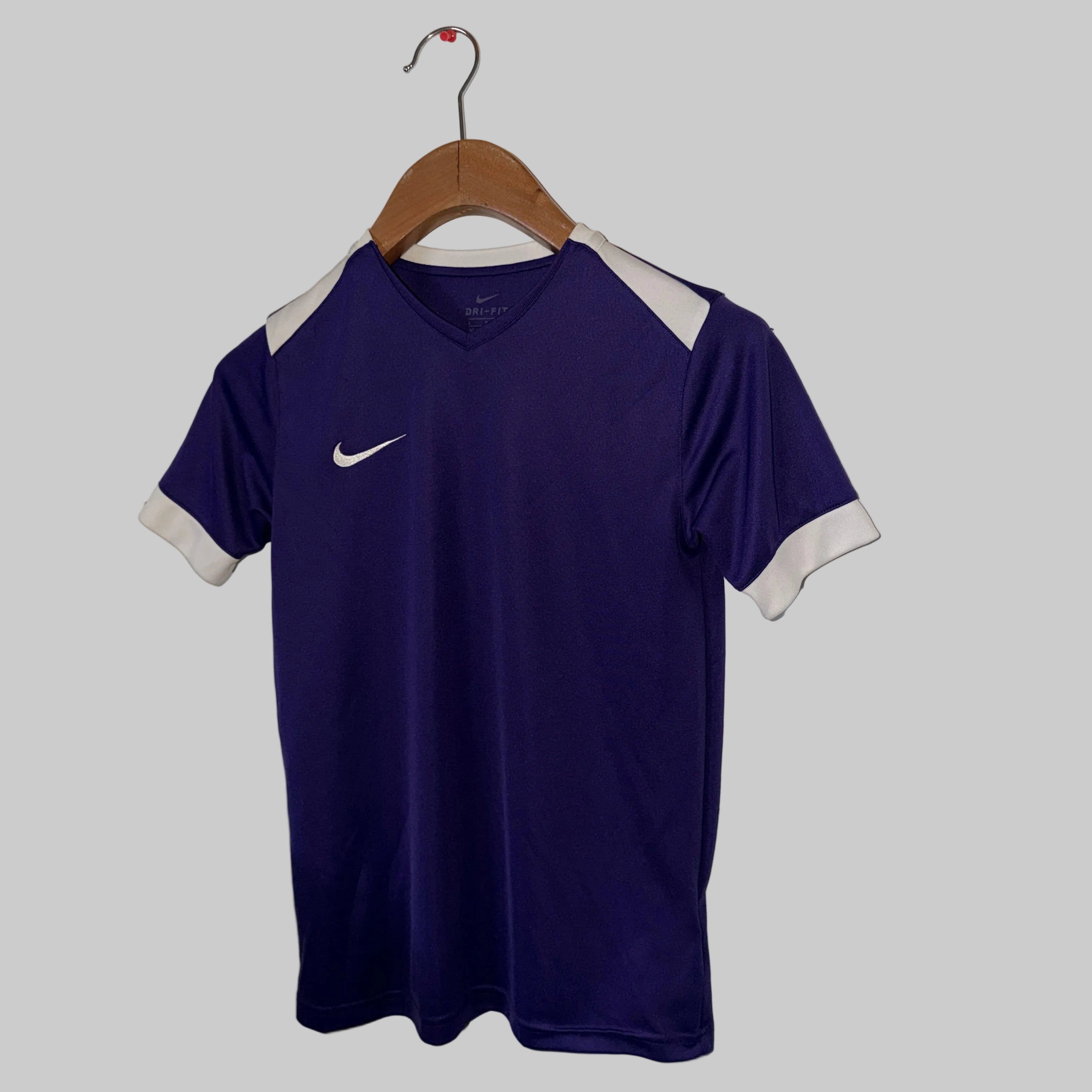 Purple sports jersey with white accents on a hanger against a white wall.