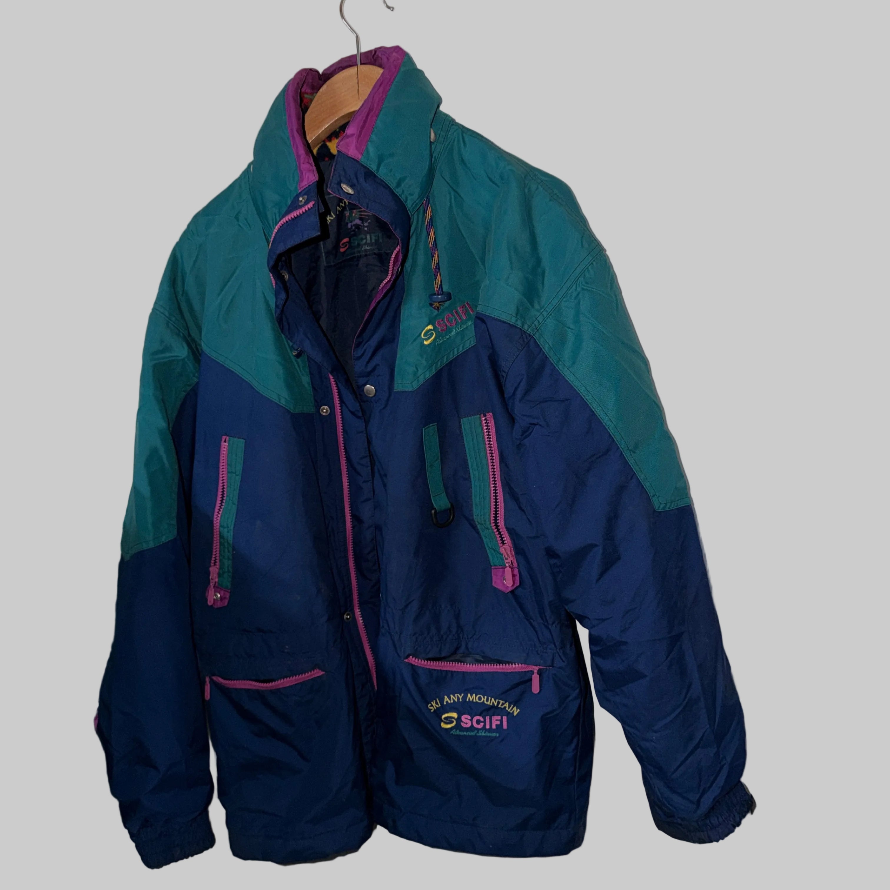 Two-tone blue and green jacket with pink accents hanging on a white wall.