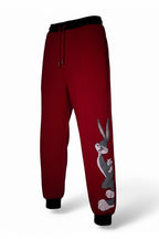 A pair of red jogging pants with an iconic cartoon character printed on the side, displayed on a hanger.