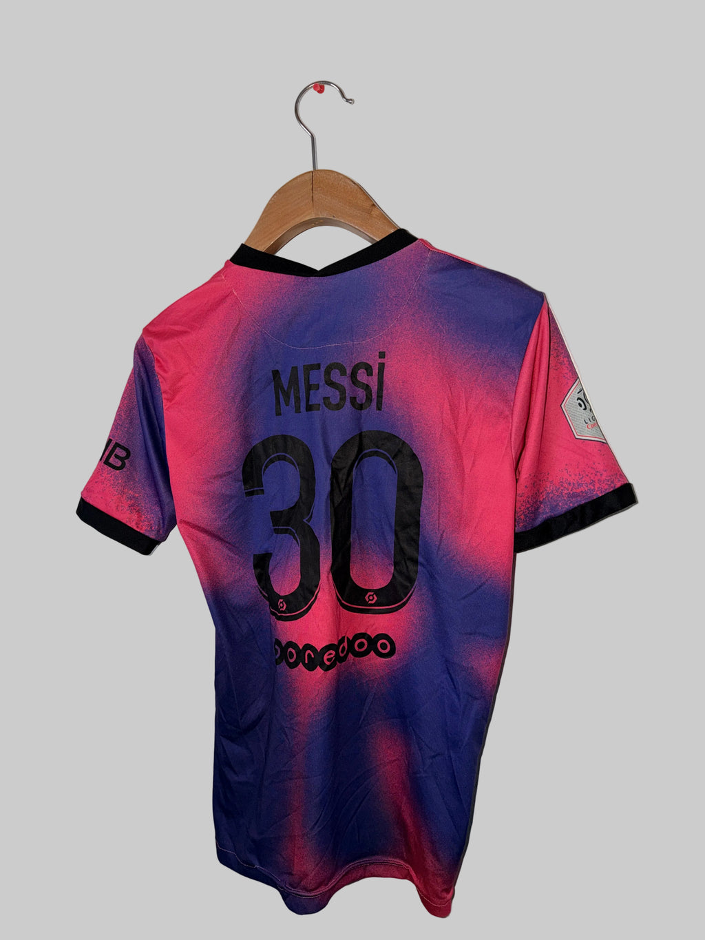 Pink and blue sports jersey with 'Messi 30' printed on it, hanging against a white wall.