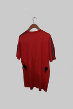 Red shirt with black accents on a hanger against a white wall.