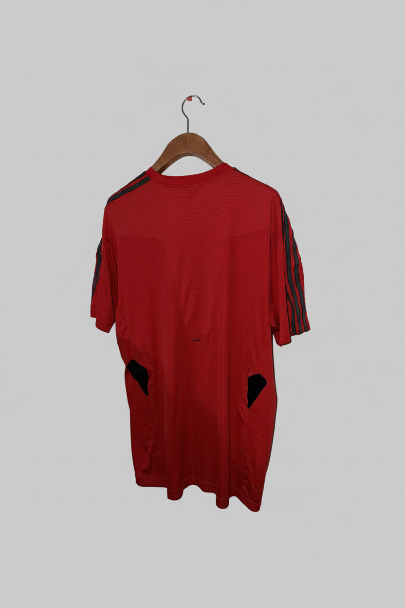 Red shirt with black accents on a hanger against a white wall.