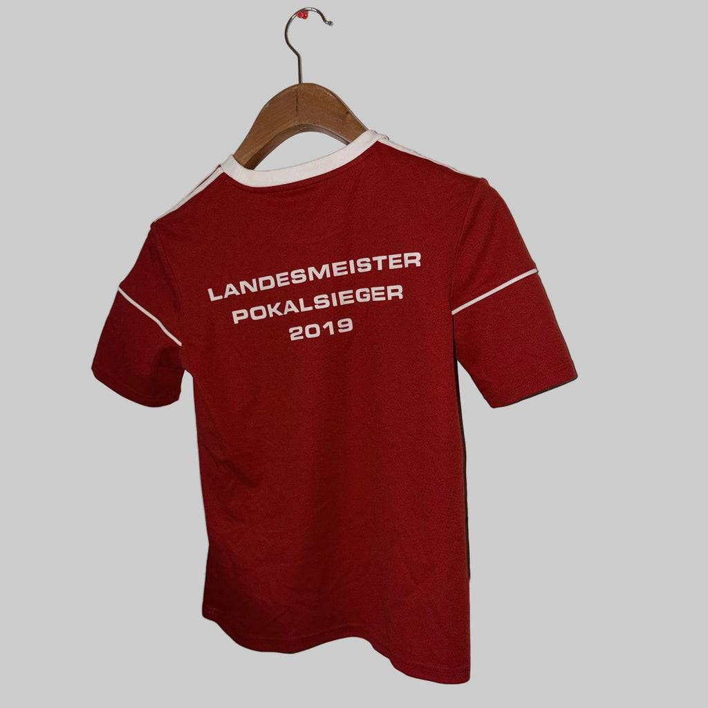 Red t-shirt with text on a hanger against a white wall