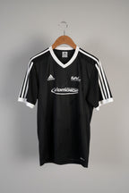 Black sports jersey with visible branding on a hanger against a white wall.