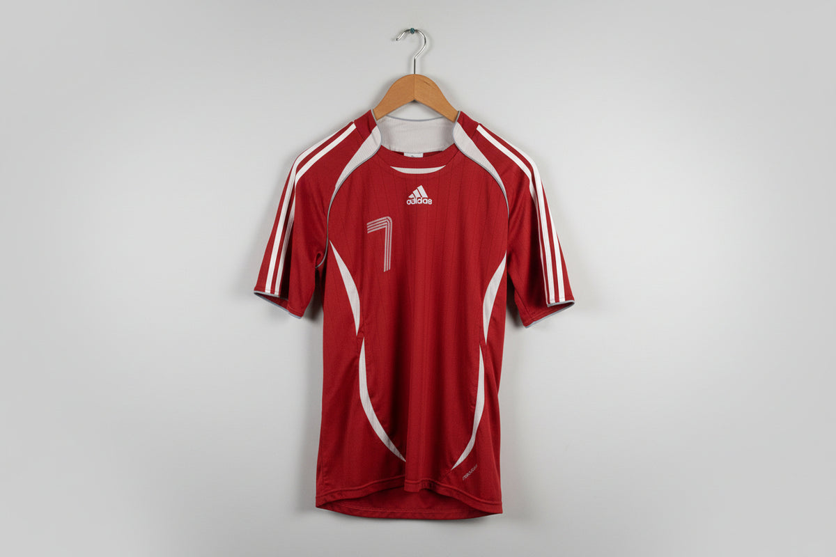 Red sports jersey with number 7 and Adidas logo on a hanger against a white wall.