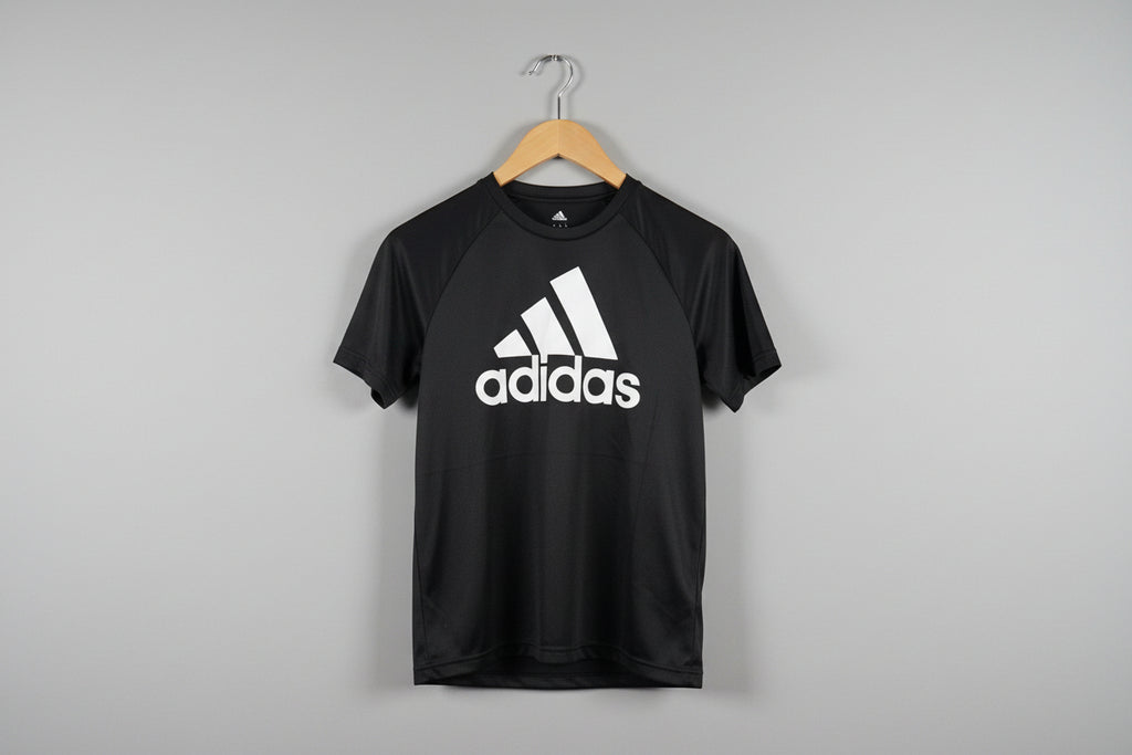 Black Adidas t-shirt on a wooden hanger against a textured white wall.